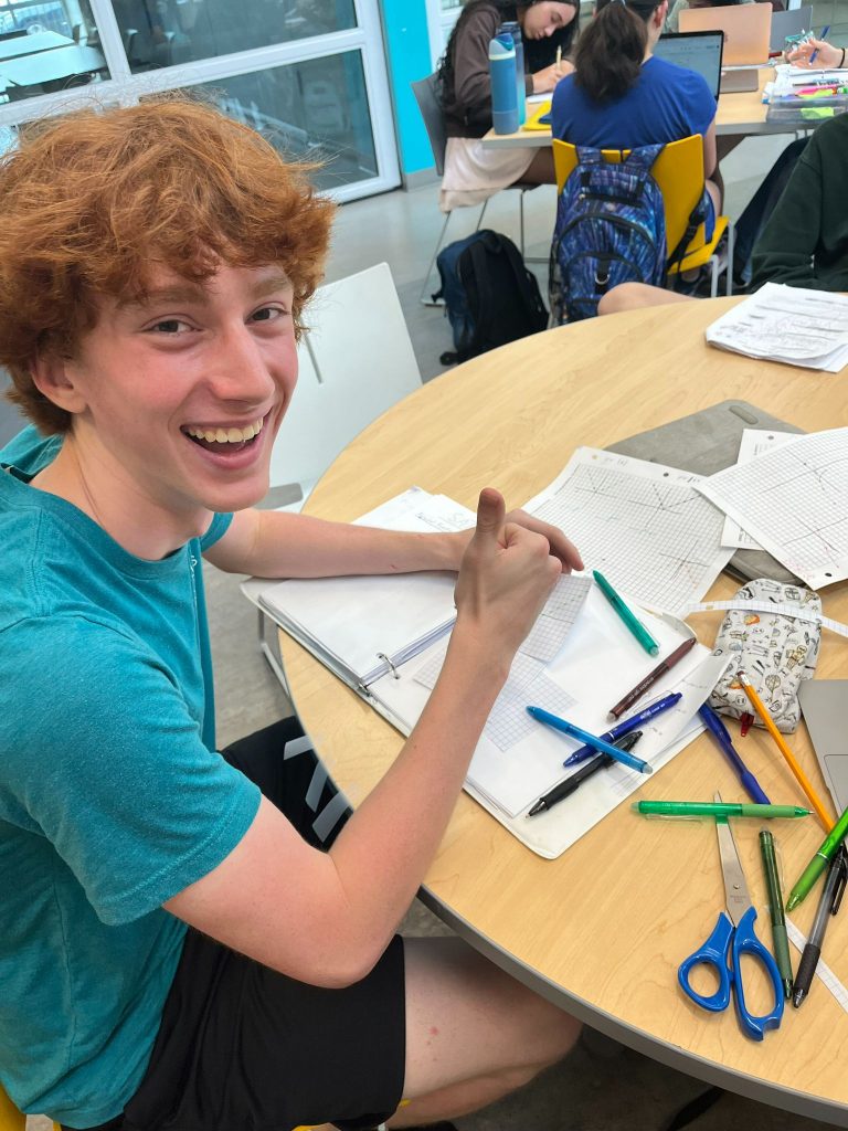 student giving a thumbs up at a desk doing math